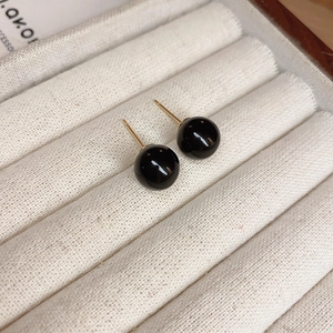 Macro view of minimalist black sphere stud earrings with gold pins on jewelry tray