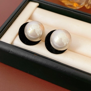 Close-up of white plush pearl earrings on beige velvet lining of a premium leather box