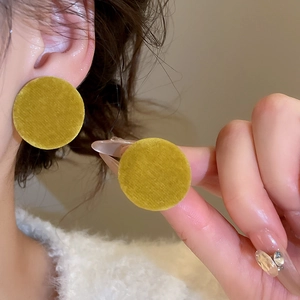 Detail showing yellow velvet round stud earrings worn by a model for a soft texture look
