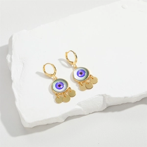 Detail of gold Evil Eye earrings with blue resin center and metal fringe on stone