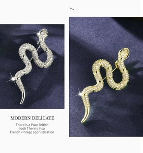 Close-up of gold and silver snake brooches with sparkling zircon on blue texture