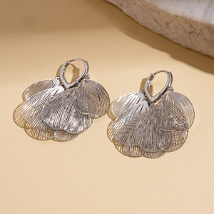 Detailed view of silver hollow leaf hoop earrings on a warm textured stone background