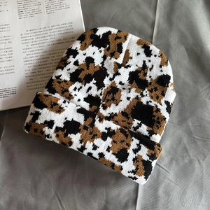 Close-up of the thick knit texture on a black and white cow pattern beanie hat