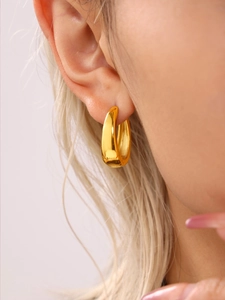 Close-up of a polished gold geometric oval earring worn by a model in a minimal setting