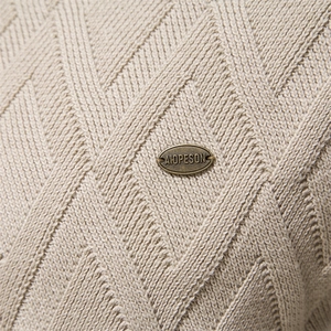 Macro detail of beige cotton knit sweater showing diamond patterns and metal logo tag