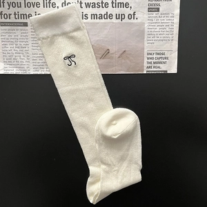 Detailed texture of white knit socks with black bow embroidery on a newspaper background