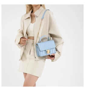 Close-up of light blue quilted crossbody bag with golden twist lock on a white outfit