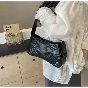 Detail of black baguette bag with flame texture and silver buckles on model