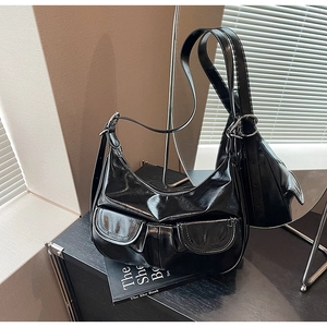 Detail of black glossy leather shoulder bag featuring dual front pockets with metal buckles