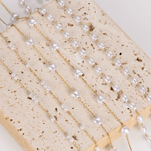 Elegant gold chain necklace with interspersed white heart and oval pearls on stone