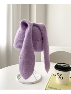 Detail of a purple knitted beanie with long rabbit ears on a white minimalist stand