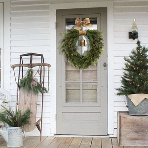 Detail of a spring wreath with pine cones, burlap bow and bells on a white door