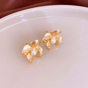 Macro shot of gold floral earrings with textured petals and center pearl on a ceramic plate