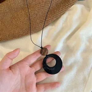Macro d'un long collier avec un anneau en acrylique noir et un disque en bois naturel