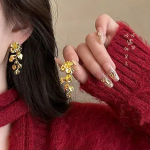 Detailed view of long gold textured floral earrings worn against a red sweater