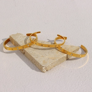 Macro detail of three 18K gold-plated bangles with star engravings and zircon stones