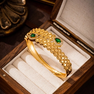 Macro view of gold vintage bangle with green teardrop stones in a luxury wooden box