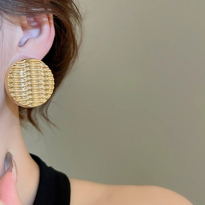 Close-up of gold round acrylic earrings featuring minimalist wave textured geometric design
