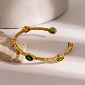 Gold plated stainless steel hammered bangle with green zircon stones on stone background