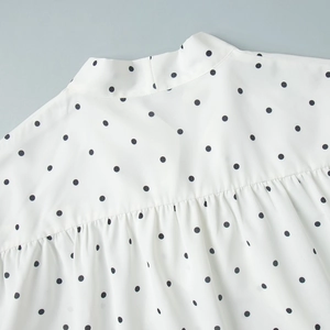 Detailed view of the standing collar and pleated shoulder on this white polka dot blouse
