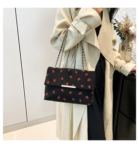 Detail of strawberry corduroy crossbody bag with gold chain strap on a trench coat