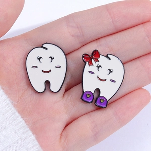 Close-up of cute cartoon tooth enamel pins with smiling faces held by hand for scale
