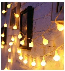 Detail of warm white LED globe string lights hanging on white brick wall for cozy decor