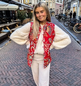 Outdoor street style view of a red printed quilted vest paired with a white knit sweater