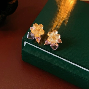 Macro detail of floral earrings with soft yellow petals and purple crystal drop pendants