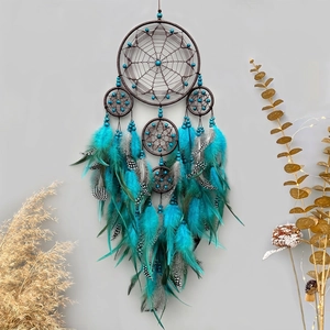 Handmade bohemian dreamcatcher with peacock blue feathers and wooden beads on gray wall