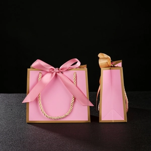 Detail of pink paper gift bag with golden border and decorative ribbon bow