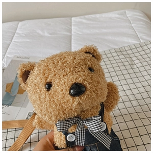 Detail of plush brown teddy bear bag wearing denim overalls with a checkered bow tie