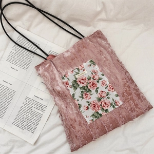 Detail of pink velvet tote bag with floral patch and black rope handles on white fabric