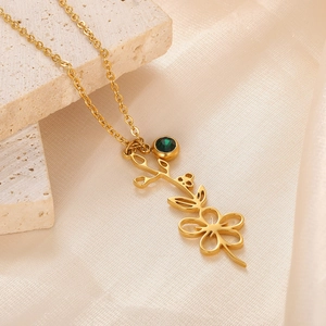Macro shot of 18k gold-plated necklace with floral pendant and green gemstone on silk