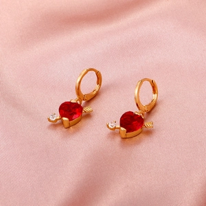 Macro detail of gold-tone heart earrings with red zircon and sparkling cupid arrow