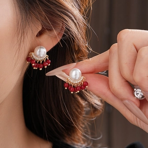 Detail shot of model wearing pearl earrings with red beaded tassels and gold metal accents