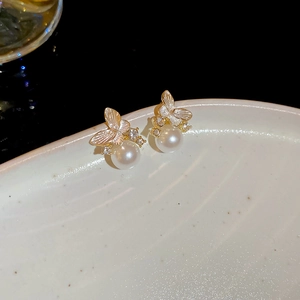 Macro shot of gold butterfly pearl earrings with brushed texture and zircon details