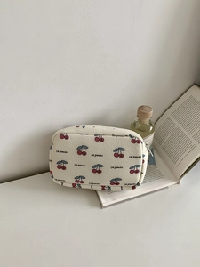 Detail of canvas cosmetic bag with cherry print resting on a book with perfume