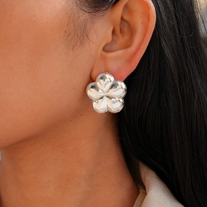 Close-up of a large silver metallic flower stud earring with a polished mirror finish