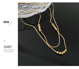 Macro detail of gold-plated snake chain necklace with spherical beads on reflective background