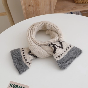 Detailed close-up of beige knitted scarf with grey color-blocking on a wooden table