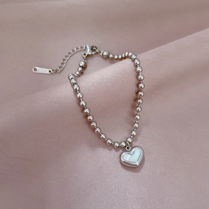 Detail of silver heart shell pendant beaded bracelet on soft pink fabric background