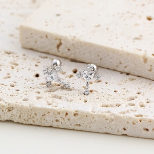 Detail of S925 silver cross earring with heart-shaped zircon on beige stone texture