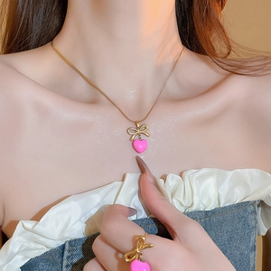 Vue détaillée du collier et de la bague avec nœud rose en forme de cœur portés par un modèle