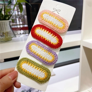 Detail of four handmade crochet hair clips in pink, red, purple and green on a white card