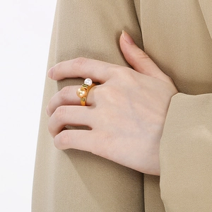 Elegant gold stainless steel ring with double pearls worn on hand against beige fabric