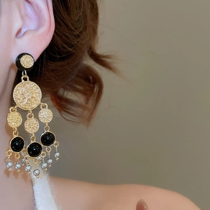 Gros plan de boucles d'oreilles vintage dorées avec perles noires et pompons de perles