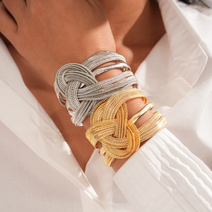 Detailed view of layered gold and silver braided chain knot bracelets on model's wrist