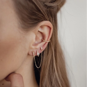 Close-up of gold ear cuff and rectangle zircon stud earrings set with chain