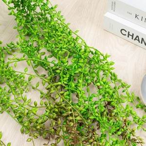 Detailed overhead view of green artificial succulent vines on a light wood background